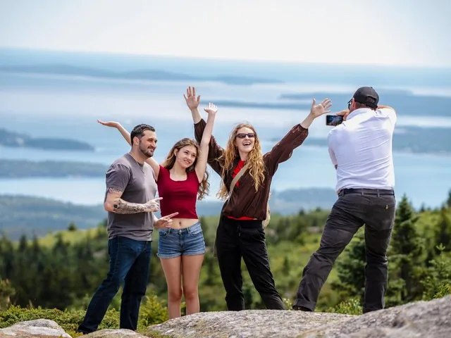 Gruppe von Menschen, die auf einer felsigen Hügelkuppe mit Blick aufs Meer Fotos machen.