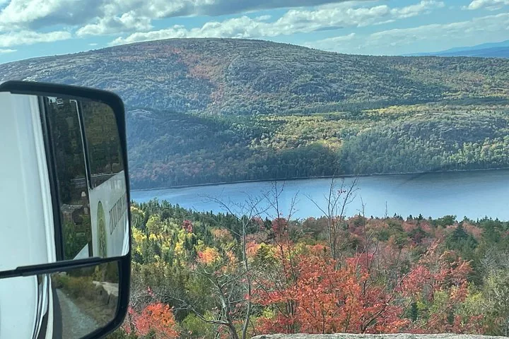 Blick aus einem Fahrzeug auf bewaldete Hügel, einen See und Herbstfarben.