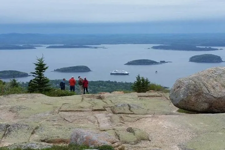 People looking at islands and a cruise ship from a rocky hilltop.